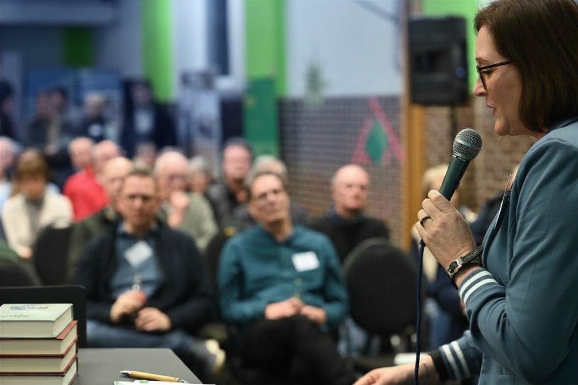 Mel Stagg reading from her work into a microphone, an audience listening