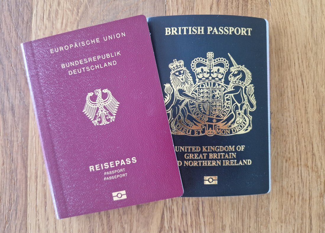 A German and a British passport lying side by side on a wooden table